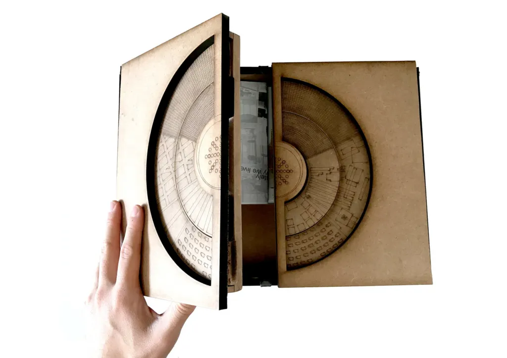 A hand opening a laser-cut model box that folds out to reveal the city plan inside